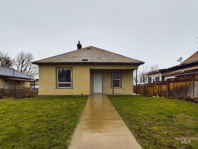 rear view of property with a chimney, fence, a lawn, and stucco siding