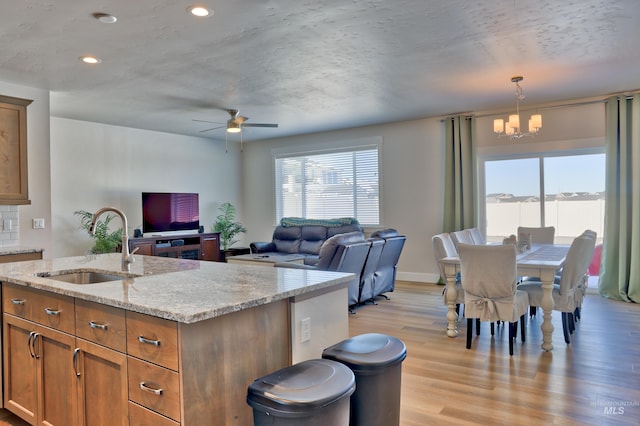 kitchen featuring sink, light stone counters, decorative light fixtures, an island with sink, and light hardwood / wood-style floors