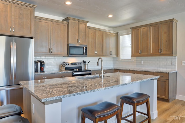 kitchen with stainless steel appliances, stone countertops, sink, and a center island with sink