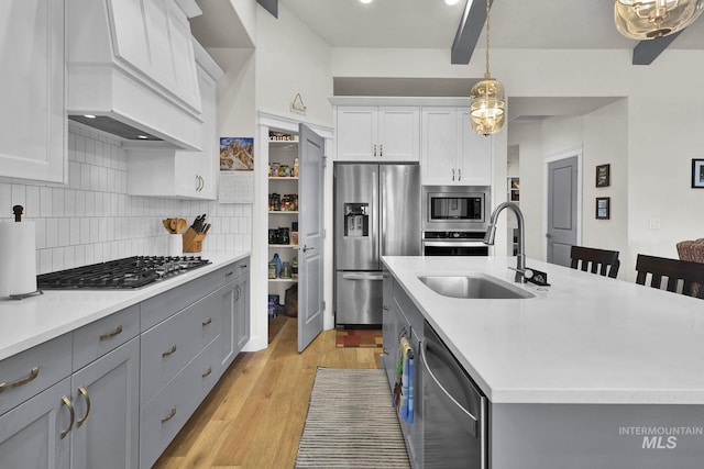 kitchen featuring gray cabinets, decorative backsplash, appliances with stainless steel finishes, light wood-style floors, and a sink