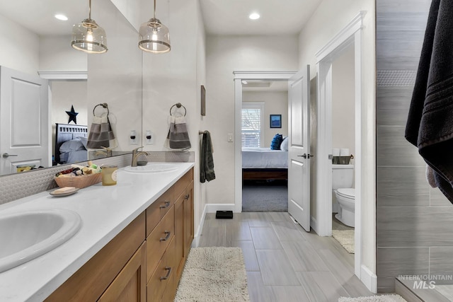 ensuite bathroom featuring double vanity, ensuite bath, toilet, and a sink