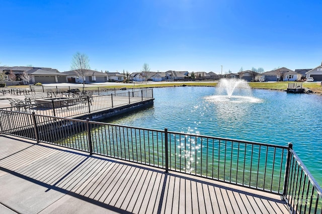 view of dock with a water view, fence, and a residential view