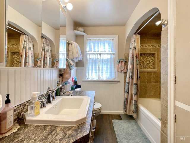 bathroom featuring vanity, shower / tub combo with curtain, toilet, a wainscoted wall, and wood finished floors