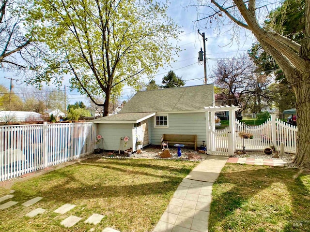 rear view of property featuring a fenced backyard, roof with shingles, a yard, and a gate