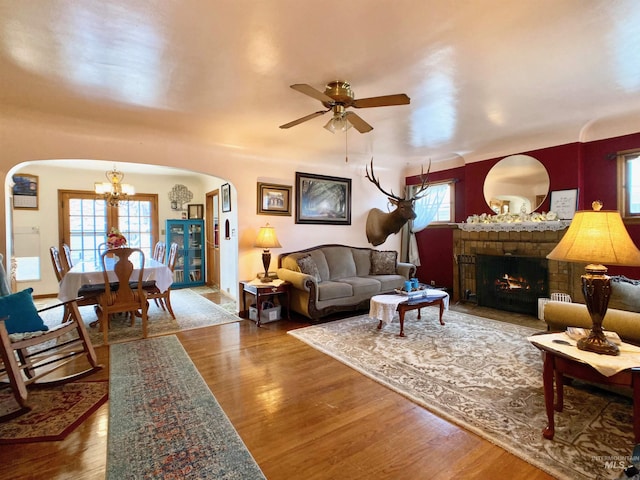 living room featuring arched walkways, plenty of natural light, wood finished floors, and ceiling fan with notable chandelier