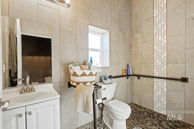 bathroom featuring tiled shower, vanity, tile walls, tile flooring, and toilet