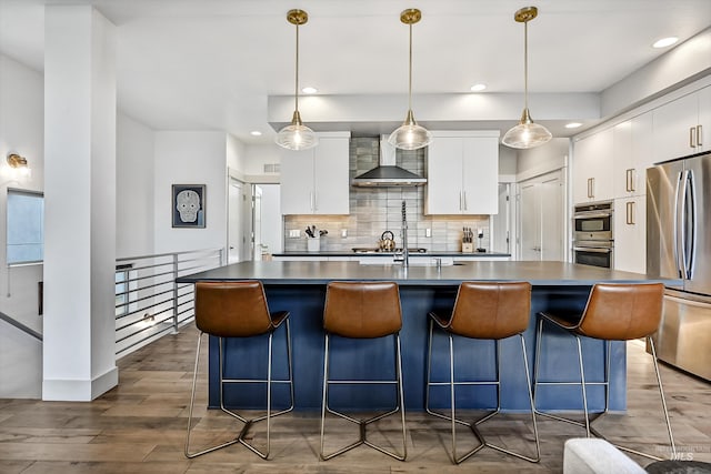 6420 W Glencrest Ln, Boise, ID 83714 - kitchen featuring stainless steel appliances, backsplash, wood finished floors, wall chimney range hood, and an island with sink