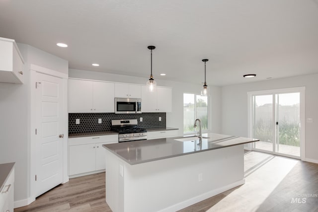 kitchen with white cabinetry, sink, stainless steel appliances, decorative light fixtures, and a center island with sink