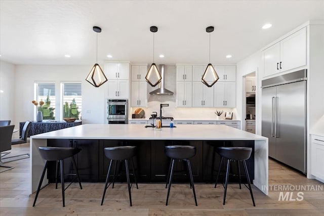 1093 N Morehouse Ave, Eagle, ID 83616 - kitchen featuring light countertops, wall chimney exhaust hood, white cabinetry, light wood-style flooring, and appliances with stainless steel finishes
