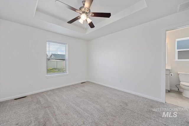 unfurnished bedroom featuring visible vents, a raised ceiling, baseboards, and light colored carpet