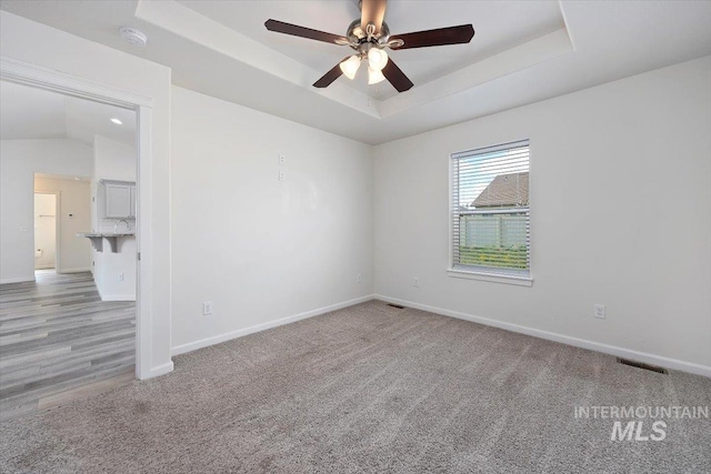 unfurnished room featuring visible vents, baseboards, ceiling fan, light colored carpet, and a raised ceiling