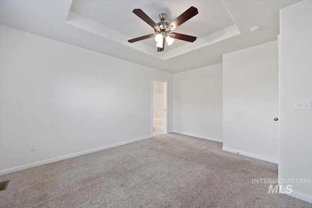 carpeted empty room with baseboards, a ceiling fan, and a tray ceiling