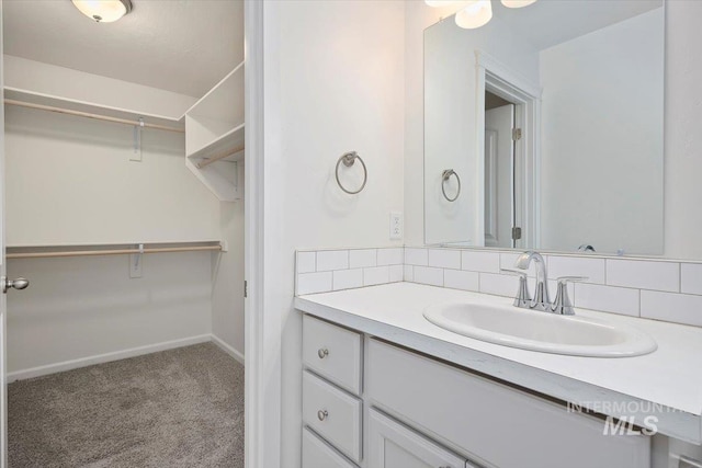 bathroom featuring a walk in closet, baseboards, backsplash, and vanity