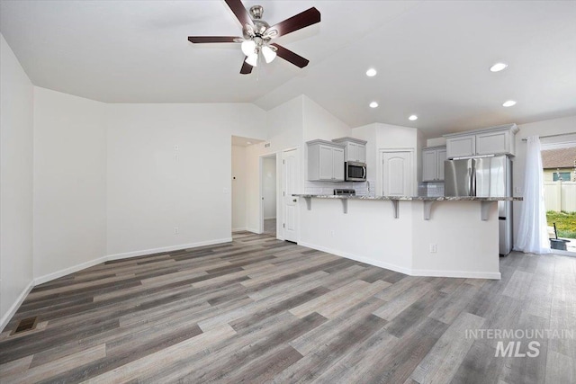 kitchen with ceiling fan, a breakfast bar area, light stone countertops, lofted ceiling, and stainless steel appliances