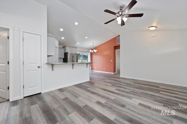 unfurnished living room with baseboards, light wood-style flooring, ceiling fan with notable chandelier, and lofted ceiling