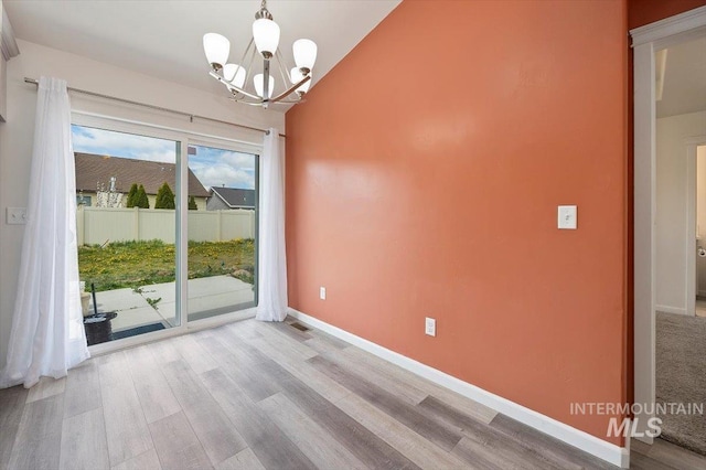 unfurnished dining area with an inviting chandelier, baseboards, wood finished floors, and visible vents