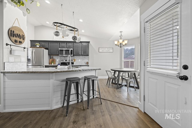 kitchen with lofted ceiling, gray cabinets, appliances with stainless steel finishes, a notable chandelier, and dark hardwood / wood-style flooring