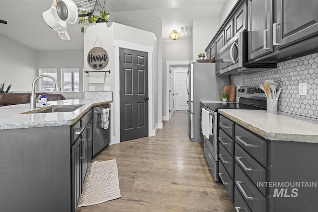 kitchen featuring light stone countertops, appliances with stainless steel finishes, decorative backsplash, sink, and light hardwood / wood-style flooring