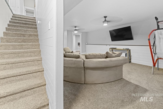 carpeted living room featuring ceiling fan and wooden walls