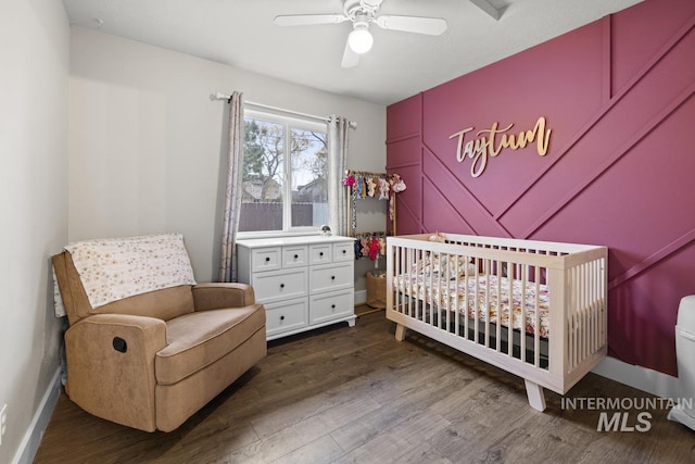 bedroom featuring a crib, ceiling fan, and dark wood-type flooring