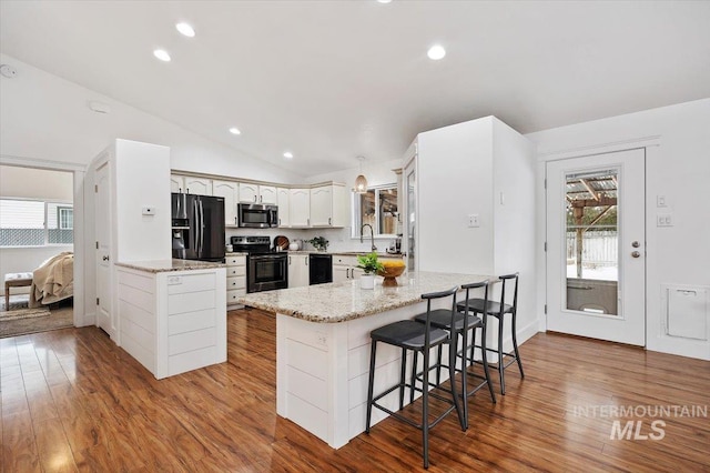 kitchen featuring vaulted ceiling, a kitchen breakfast bar, black appliances, kitchen peninsula, and white cabinets