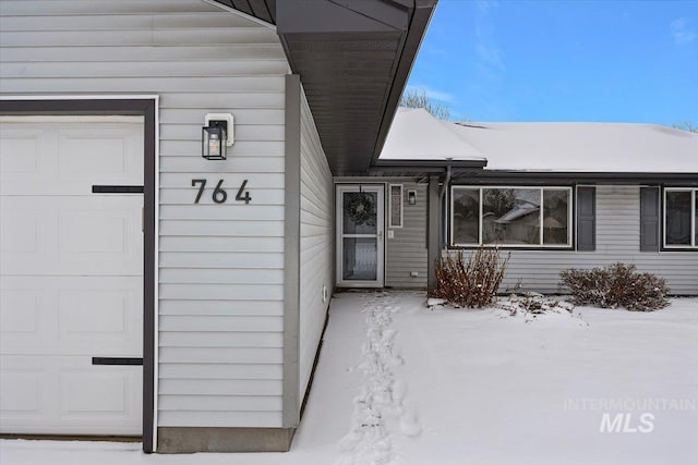 snow covered property entrance featuring a garage