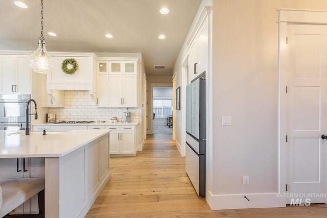 kitchen featuring hanging light fixtures, backsplash, stainless steel appliances, and white cabinets