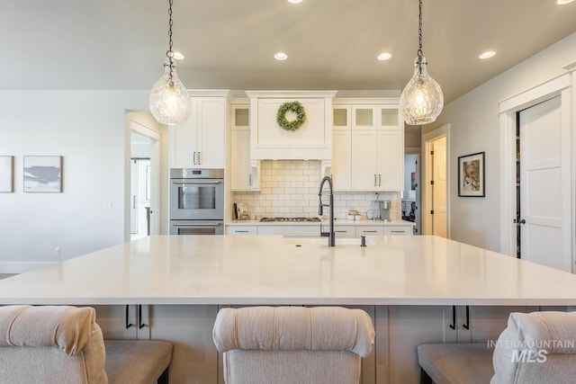 kitchen with a breakfast bar, sink, white cabinetry, tasteful backsplash, and a large island