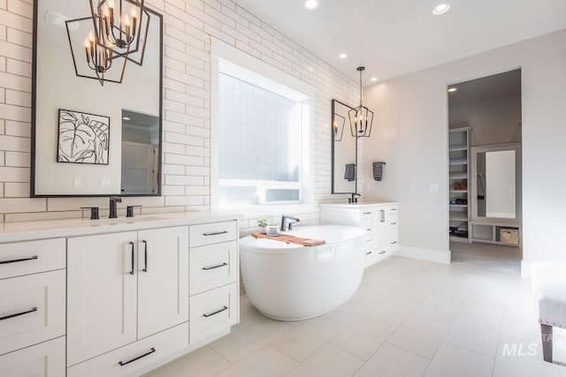 bathroom with an inviting chandelier, a tub to relax in, vanity, and tile patterned flooring