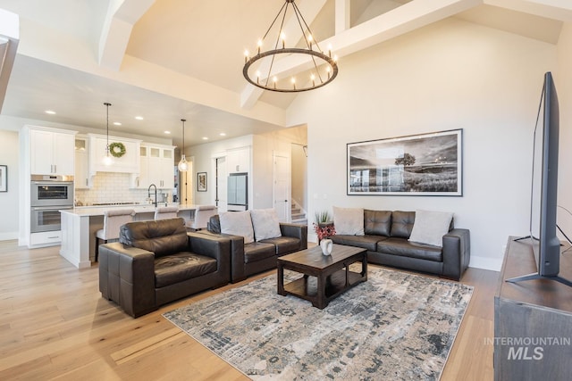 living room featuring sink, light hardwood / wood-style flooring, beam ceiling, high vaulted ceiling, and a chandelier