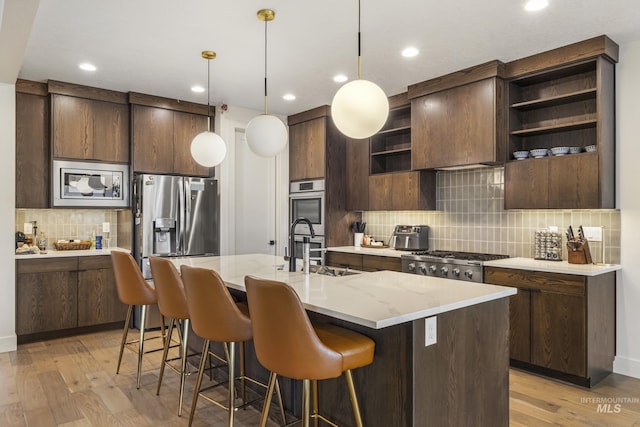 kitchen featuring appliances with stainless steel finishes, dark brown cabinets, light wood-style floors, open shelves, and a sink