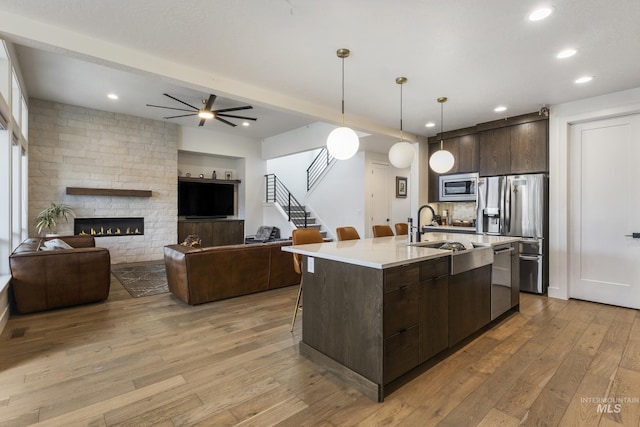 kitchen with dark brown cabinetry, a sink, appliances with stainless steel finishes, light wood-type flooring, and modern cabinets