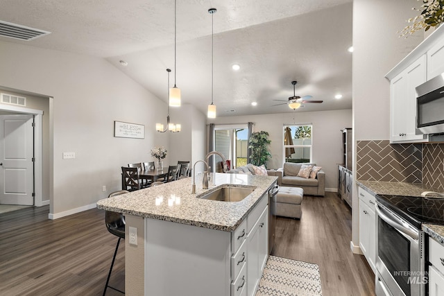 kitchen with appliances with stainless steel finishes, pendant lighting, sink, white cabinets, and a kitchen island with sink