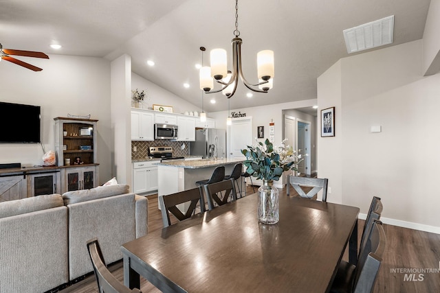 dining area featuring vaulted ceiling, dark wood-type flooring, and ceiling fan with notable chandelier