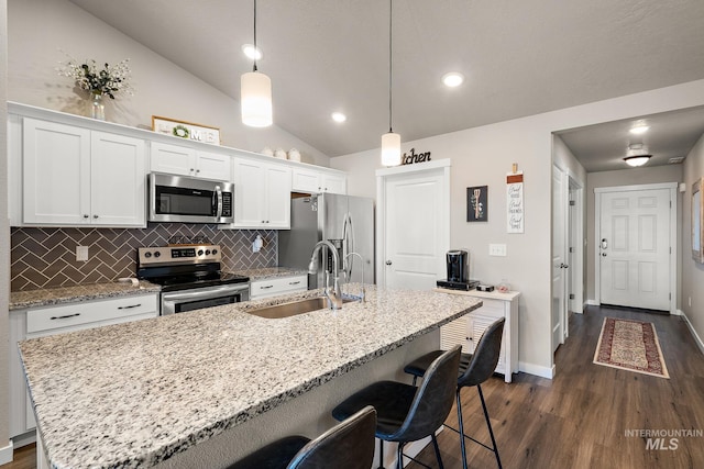 kitchen featuring appliances with stainless steel finishes, decorative light fixtures, sink, white cabinets, and a center island with sink