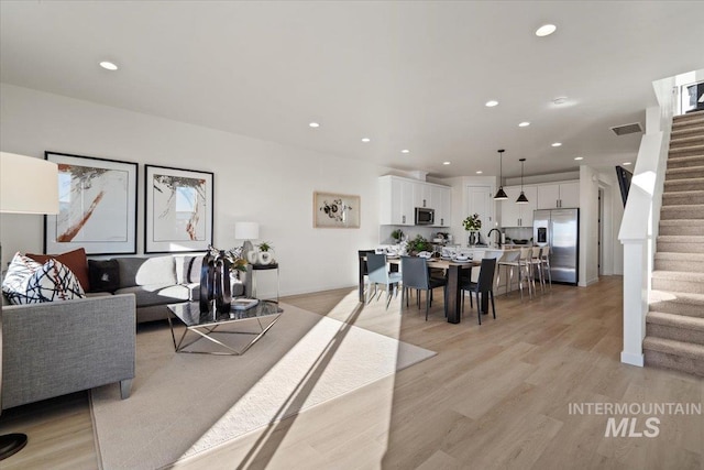 living area featuring light wood finished floors, visible vents, baseboards, stairway, and recessed lighting