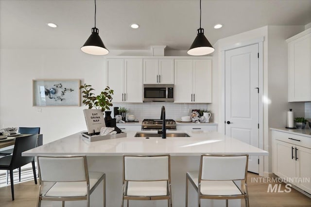 kitchen with stainless steel microwave, backsplash, white cabinetry, and light countertops