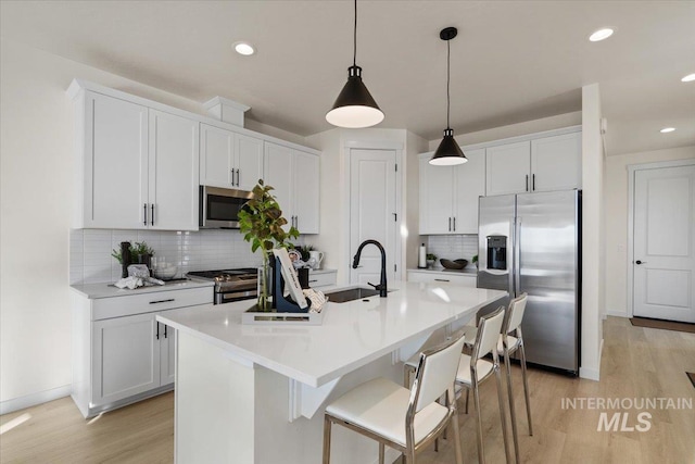 kitchen with light wood finished floors, an island with sink, appliances with stainless steel finishes, white cabinets, and a sink