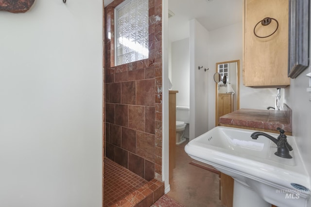 bathroom with toilet, tiled shower, and sink