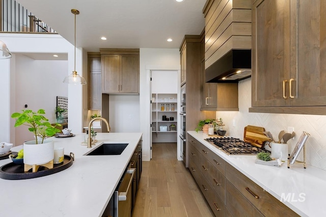 kitchen with decorative light fixtures, stainless steel appliances, tasteful backsplash, sink, and light wood-type flooring