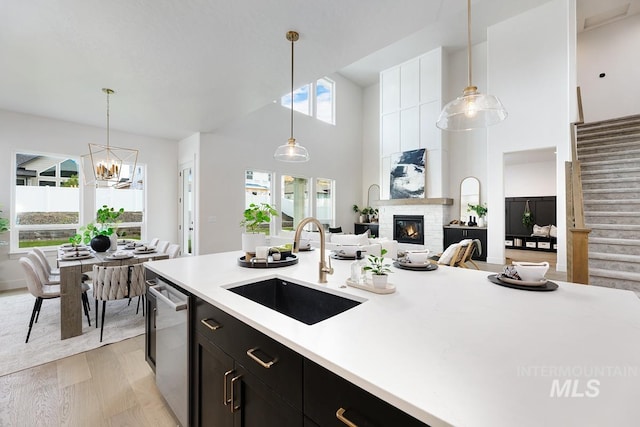 kitchen with a towering ceiling, decorative light fixtures, light hardwood / wood-style floors, sink, and stainless steel dishwasher