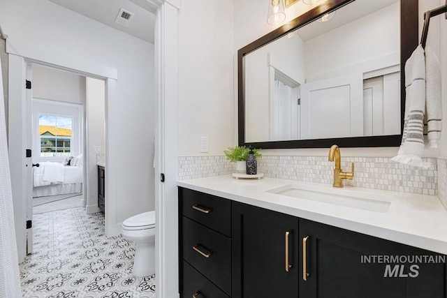 bathroom featuring toilet, vanity, and backsplash