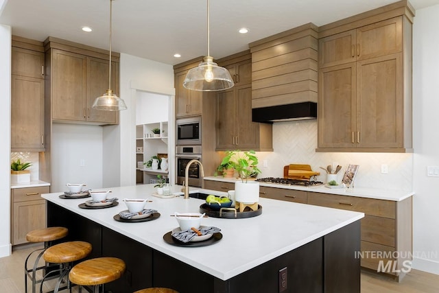 kitchen featuring a kitchen bar, light hardwood / wood-style floors, appliances with stainless steel finishes, and an island with sink