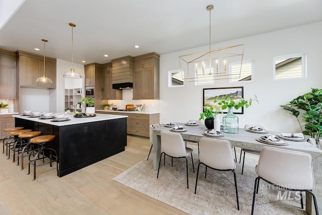 kitchen featuring a notable chandelier, pendant lighting, light hardwood / wood-style flooring, a kitchen island with sink, and a breakfast bar area