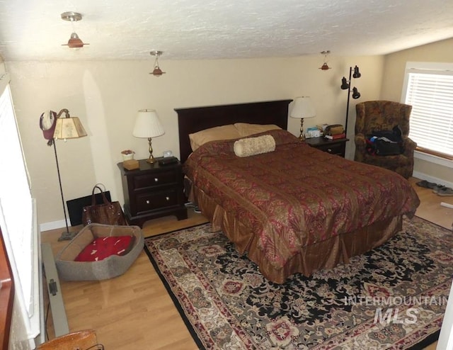 bedroom with a textured ceiling, baseboards, and wood finished floors