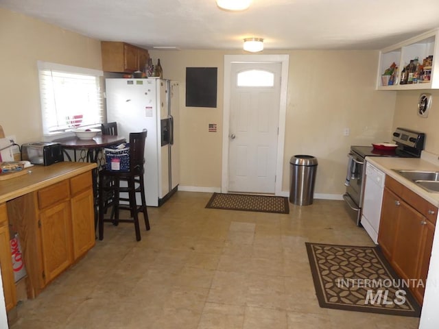 kitchen featuring baseboards, light countertops, white appliances, and brown cabinets