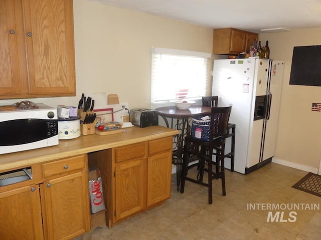 kitchen featuring white appliances, baseboards, light countertops, brown cabinets, and light floors