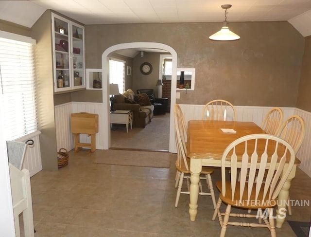 dining room featuring arched walkways, a wainscoted wall, and vaulted ceiling