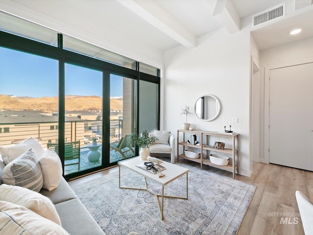 living room with a mountain view, plenty of natural light, beamed ceiling, and light wood-type flooring