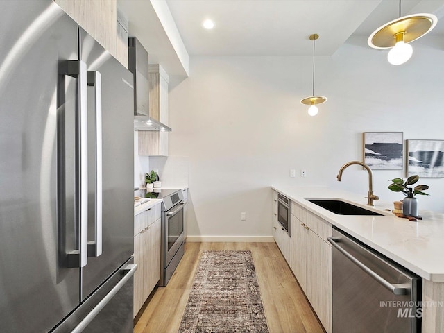 kitchen featuring stainless steel appliances, wall chimney range hood, decorative light fixtures, light stone countertops, and sink